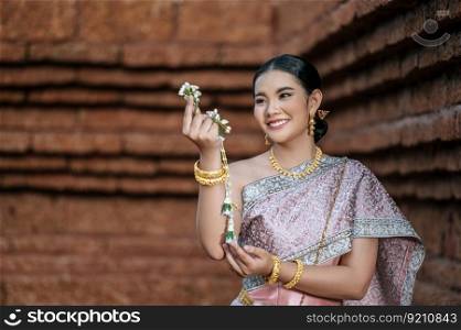 Portrait Asian charming woman wearing beautiful typical Thai dress identity culture of Thailand in ancient temple or famous place, sheholding fresh flower garland with gracefully pose, copy space