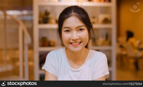Portrait Asian Chinese woman feeling happy smiling in library at university. Young undergraduate teen girl relax toothy smile looking to camera at college campus overtime at night concept.