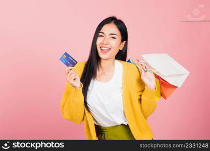 Portrait Asian happy beautiful young woman shopper smiling standing excited holding online shopping bags colorful and credit card for payment on hand in summer, studio shot isolated on pink background