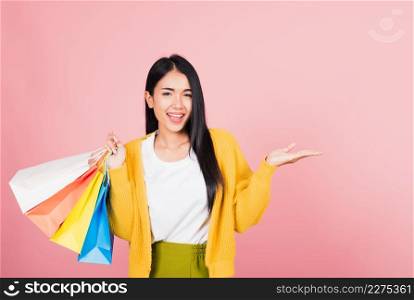 Portrait Asian happy beautiful young woman shopper smiling standing excited holding shopping bags multicolor in summer show something hand palm to copy space, studio shot isolated on pink background
