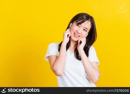 Portrait Asian of a happy beautiful young woman wear wireless earphone listening to music from smartphone having fun and dancing to sounds of favorite music studio shot isolated on yellow background