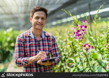 Portrait asian small business owner of orchid gardening farm, Happiness founder checking and writing, The purple orchids are blooming in the garden farm,Purple orchids in farming of bangkok, thailand.