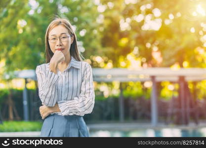 portrait Asian smart look business woman standing thinking hand at chin on green outdoor background