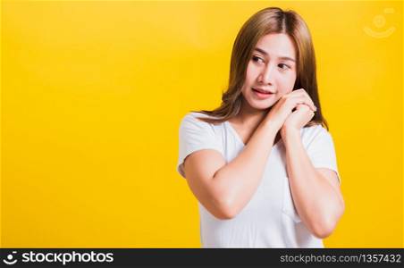 Portrait Asian Thai beautiful happy young woman smiling, screaming excited keeps two hands together near the face and looking to side, studio shot isolated on yellow background, with copy space