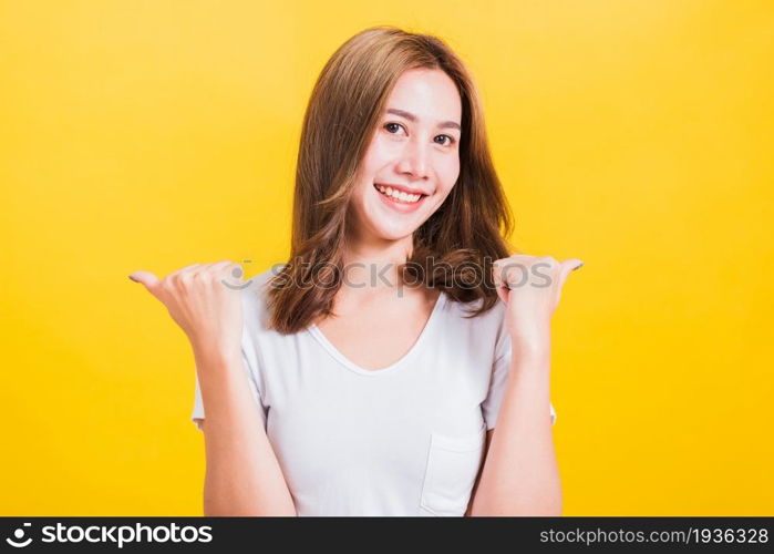 Portrait Asian Thai beautiful happy young woman smiling wear white t-shirt standing successful woman giving two thumbs up gesture sign in studio shot, isolated on yellow background with copy space