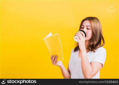 Portrait Asian Thai beautiful happy young woman standing holding drinking take away cup coffee paper and reading yellow book or diary, studio shot isolated on yellow background, with copy space