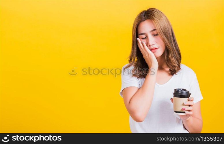 Portrait Asian Thai beautiful happy young woman standing Tired sleepy her cannot wake up and closes eyes holds take away cup coffee, studio shot isolated on yellow background, with copy space