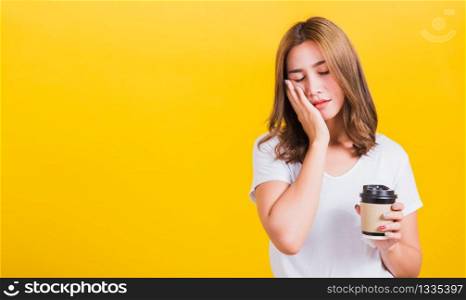 Portrait Asian Thai beautiful happy young woman standing Tired sleepy her cannot wake up and closes eyes holds take away cup coffee, studio shot isolated on yellow background, with copy space