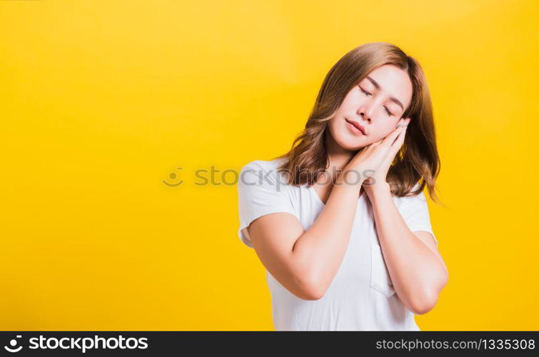 Portrait Asian Thai beautiful young woman emotions tired and sleepy her posing sleeping to dreaming with hands together near face, studio shot on yellow background, with copy space, insomnia concept