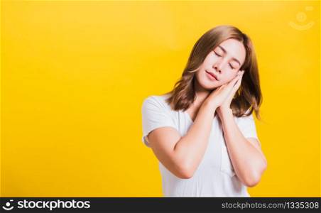 Portrait Asian Thai beautiful young woman emotions tired and sleepy her posing sleeping to dreaming with hands together near face, studio shot on yellow background, with copy space, insomnia concept