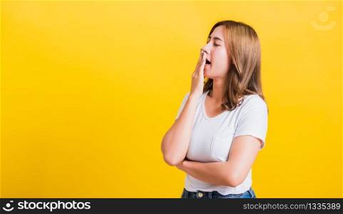 Portrait Asian Thai beautiful young woman emotions tired and sleepy her yawning close mouth open by hand, shoot a photo in the studio on yellow background, There was copy space, insomnia concept