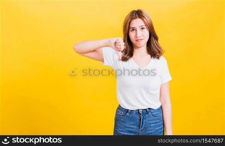 Portrait Asian Thai beautiful young woman unhappy, a negative gesture showing finger thumbs down or dislike sign, studio shot isolated on yellow background, There was copy space, rejection concept