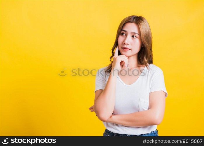 Portrait Asian Thai beautiful young woman wearing white t-shirt standing chin handle relaxed thinking about something about the question studio shot, isolated on yellow background with copy space