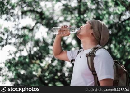 Portrait Asian traveler man with backpack drinking water from bottle in woodland with copy space. Male hiker drinking water in forest. Vacation, holiday and hobby concept.