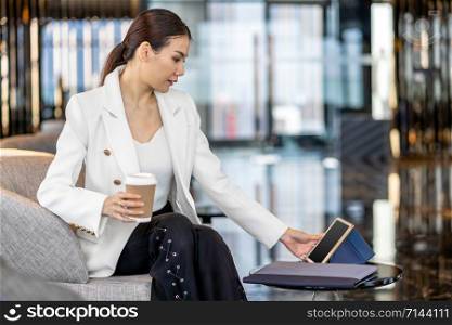 Portrait Asian woman holding paper coffee cup and using technology tablet for online shopping in modern lobby or working space, technology money wallet and online payment concept