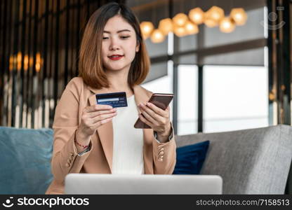 Portrait Asian woman using credit card with mobile phone, laptop for online shopping in modern lobby or working space, coffee cup, technology money wallet and online payment concept,credit card mockup