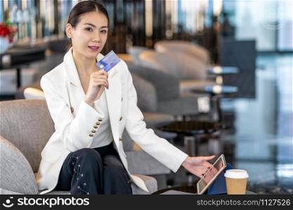 Portrait Asian woman using credit card with technology tablet for online shopping in modern lobby or working space, coffee cup, technology money wallet and online payment concept, credit card mockup