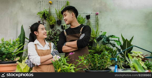 Portrait asian young gardener couple wearing apron use garden equipment and help to take care the houseplant in shop together, small business with green plant