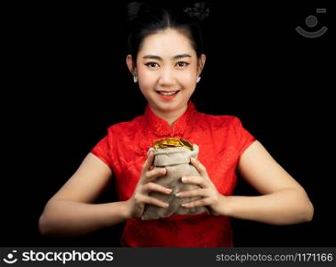 Portrait Asian young, woman red dress traditional cheongsam holding a gold coin in a sack at the black background, China Girl, Concept Chinese New Year