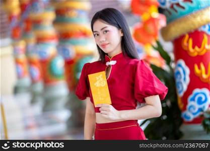 Portrait Asian young woman wearing red traditional Chinese cheongsam decoration holding yellow angpao envelopes with the Chinese text Blessings written on it Is a Good luck for Happy chinese new year