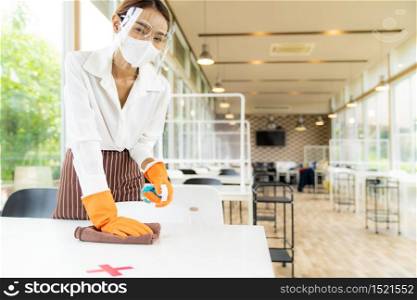 Portrait attractive asian waitress wear face mask and face shield cleaning table with alcohol and wet wipe before welcome customer. New normal hygiene restaurant concept.