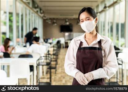 Portrait attractive asian waitress wear face with background of customers sit in social distance table in restaurant indoor. New normal restaurant lifestyle concept.