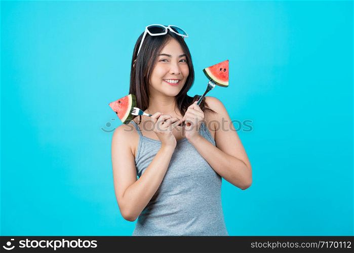 Portrait Attractive Asian young woman holding two Piece slide of watermelon and wearing fashion sunglasses on isolated blue color background, copy space and studio, diet and healthy fruit concept