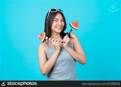 Portrait Attractive Asian young woman holding two Piece slide of watermelon and wearing fashion sunglasses on isolated blue color background, copy space and studio, diet and healthy fruit concept