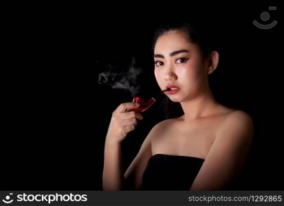 Portrait beautiful asea young women with a smoking pipe tobacco and look at the camera on the black background, Studio shot close up Image of cigarette smoke spread in lady hand
