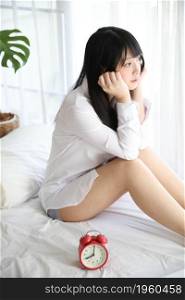 Portrait beautiful asian girl sitting with clock at white bedroom