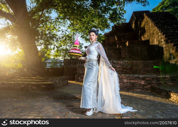 Portrait Beautiful asian woman with Thai white traditional dress costume holding Krathong and sitting in front of Pagoda temple at the ancient city Thailand,Loy Krathong Festival,Transgender model