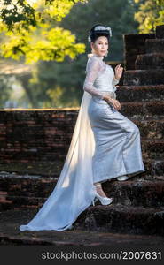 Portrait Beautiful asian woman with Thai white traditional dress costume holding Krathong and sitting in front of Pagoda temple at the ancient city Thailand,Loy Krathong Festival,Transgender model