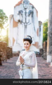 Portrait Beautiful asian woman with Thai white traditional dress saluting hands in front of Old Buddha statue Pagoda temple at the ancient city Thailand,Loy Krathong Festival,Transgender model