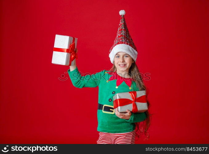 Portrait beautiful elven baby. Elf girl with gifts, Santa Claus helper on a bright red bright colored background. Copy space.. Elf girl with gifts, Santa Claus helper on a bright red bright colored background. Portrait beautiful elven baby.