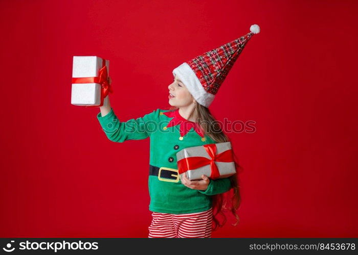 Portrait beautiful elven baby. Elf girl with gifts, Santa Claus helper on a bright red bright colored background. Copy space.. Elf girl with gifts, Santa Claus helper on a bright red bright colored background. Portrait beautiful elven baby.