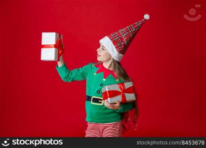 Portrait beautiful elven baby. Elf girl with gifts, Santa Claus helper on a bright red bright colored background. Copy space.. Elf girl with gifts, Santa Claus helper on a bright red bright colored background. Portrait beautiful elven baby.