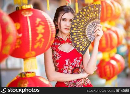 Portrait beautiful smiles Asian young woman wearing red traditional Chinese cheongsam decoration and holding with paper lanterns a Chinese Fanning for Chinese New Year Festival at Chinese shrine