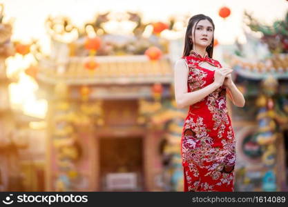 Portrait beautiful smiles Asian young woman wearing red traditional Chinese cheongsam decoration for Chinese New Year Festival at Chinese shrine in Thailand