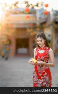 Portrait beautiful smiles Asian young woman wearing red traditional Chinese cheongsam decoration holding golden money bag for Chinese New Year Festival at Chinese shrine in Thailand