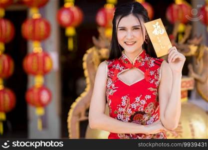 Portrait beautiful smiles Asian young woman wearing red traditional Chinese cheongsam decoration holding yellow envelopes in hand for Chinese New Year Festival at Chinese shrine in Thailand
