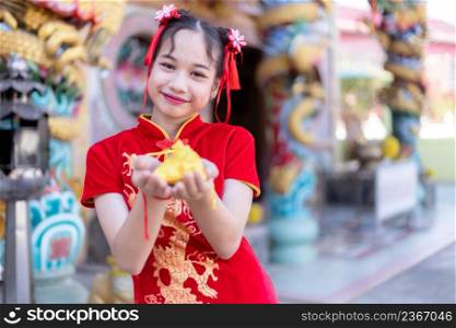 Portrait beautiful smiles Cute little Asian girl wearing red traditional Chinese cheongsam decoration focus show golden money bag for Chinese New Year Festival at Chinese shrine in thailand