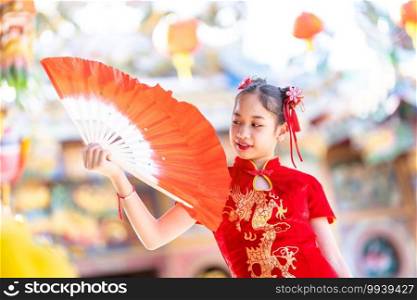 Portrait beautiful smiles Cute little Asian girl wearing red traditional Chinese cheongsam decoration and holding a Fanning for Chinese New Year Festival at Chinese shrine