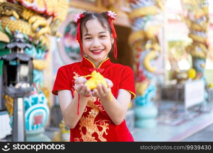 Portrait beautiful smiles Cute little Asian girl wearing red traditional Chinese cheongsam decoration holding golden money bag for Chinese New Year Festival at Chinese shrine in thailand