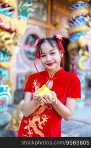 Portrait beautiful smiles Cute little Asian girl wearing red traditional Chinese cheongsam decoration focus show golden money bag for Chinese New Year Festival at Chinese shrine in thailand