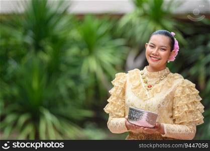 Portrait beautiful woman in Songkran festival with Thai Traditional costume in the temple holding water bowl and smile. Thailand culture with Water festival