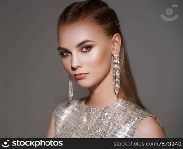 Portrait beautiful woman with jewelry. Brunette girl with long smooth hair. Beauty fashion. Eyelashes. Cosmetic eyeshadow. Care and beauty hair products. Model in a silver dress