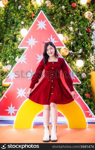 Portrait beautiful young asian woman red dress costume and Christmas greeting picture parcel decoration on Christmas tree light circular bokeh background Decoration During Christmas and New Year.