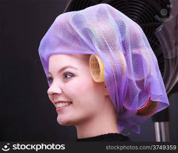 Portrait beautiful young woman in beauty salon. Blond girl with hair curlers rollers by hairdresser. Hairstyle.