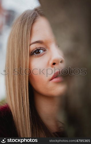 Portrait blonde girl next to a tree trunk in a park