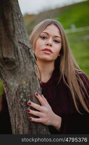 Portrait blonde girl next to a tree trunk in a park